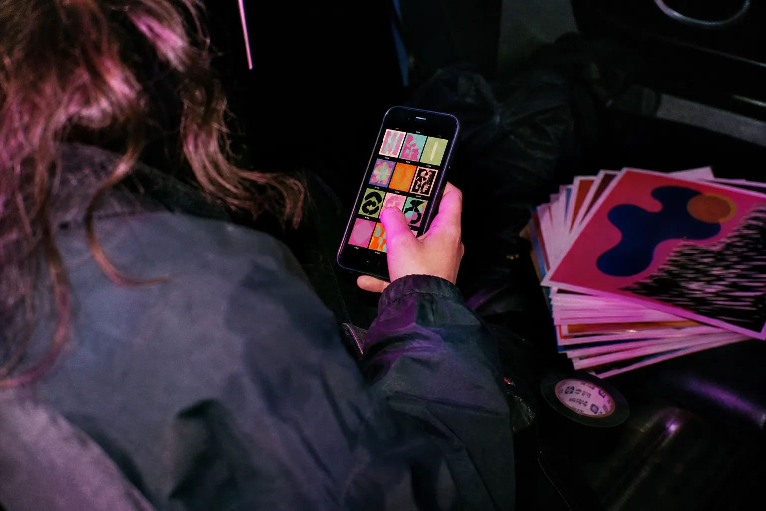 Over the shoulder of a promoter scrolling a grid of show posts on a phone, a stack of printed flyers beside them